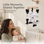 Mother and baby looking at a black and white dinosaur baby mobile