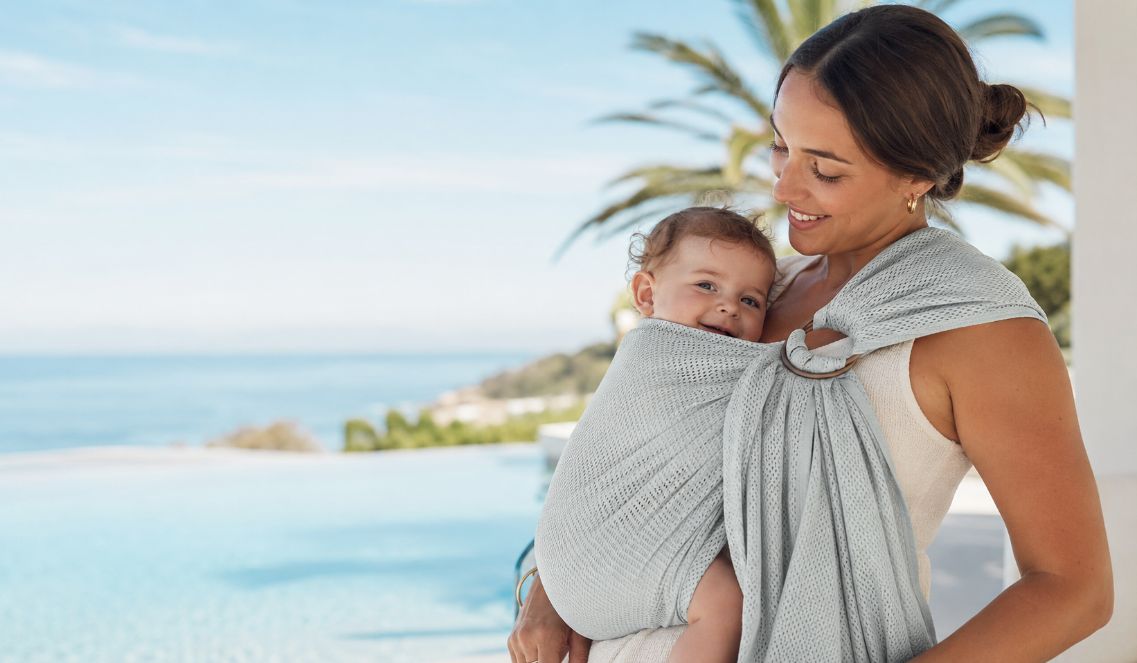 Parent carrying baby in a water ring sling beside a pool